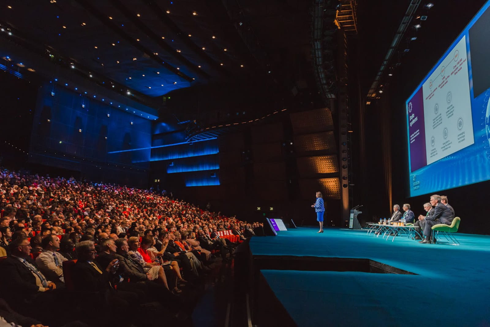 Female presenter giving keynote speech to packed auditorium in Paris.